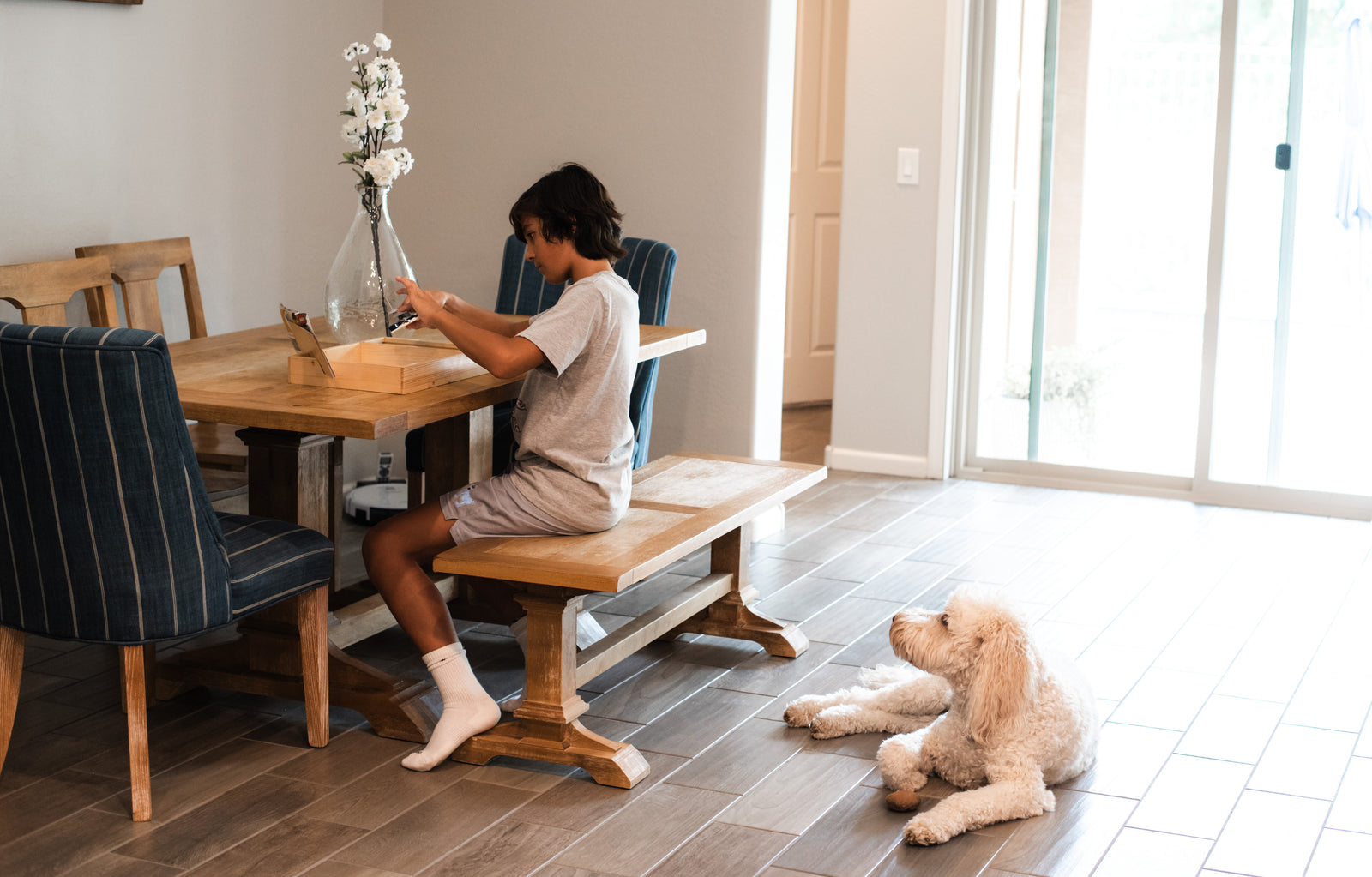 Child sitting at a table building a set using the TRA Company tray while a dog looks on. 